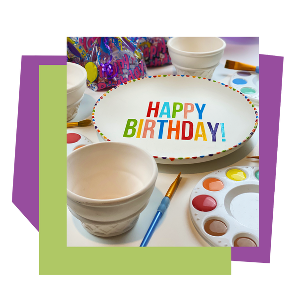 Painted ceramic plate with 'Happy Birthday!' text, surrounded by painting supplies for a party to go on a white background.