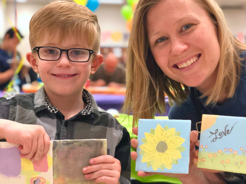 Child and adult holding hand painted tiles with a sunflower design at an off-site pottery painting event