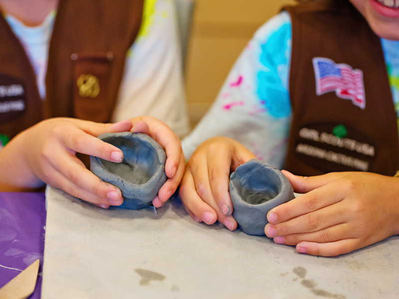 Two pairs of hands holding gray clay pots, with a focus on the hands and pots.