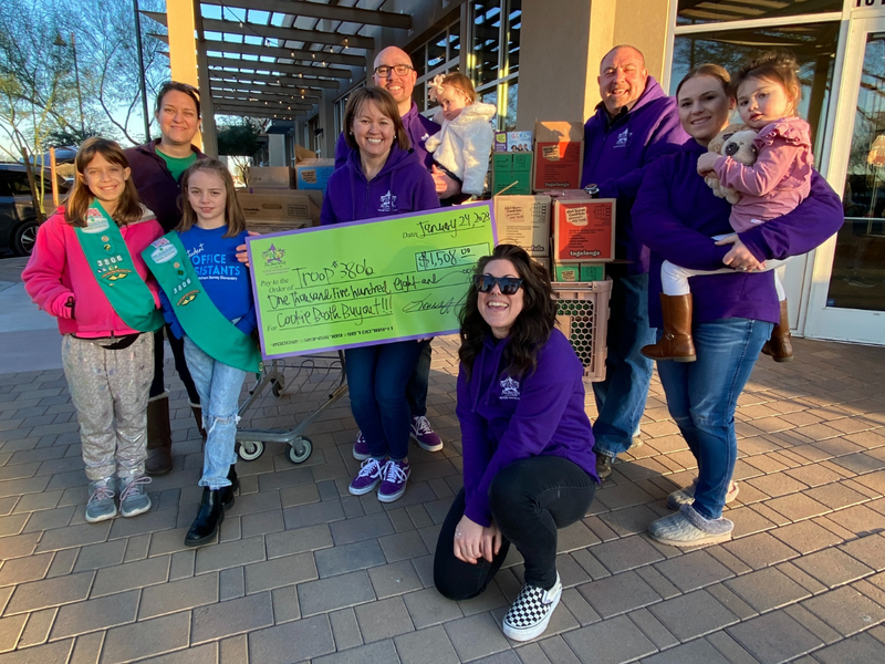 Group of people, including children and adults, holding a large check outdoors.