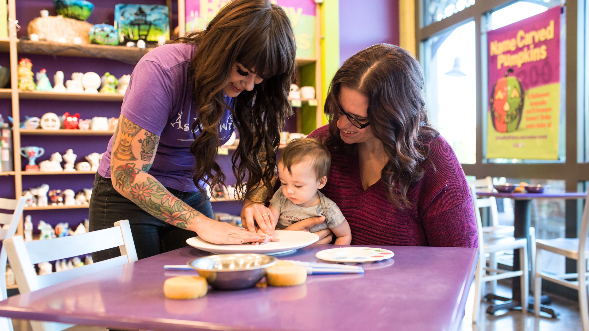 Two women placing a child's handprint on a plate