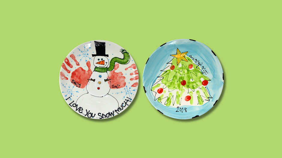 Two decorative plates with a snowman and Christmas tree hand prints on a green background