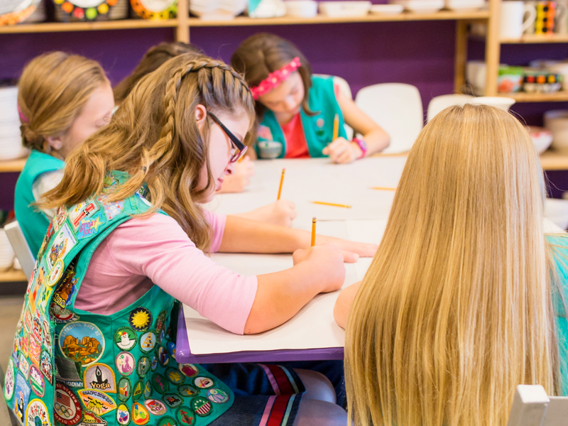 Girl Scouts in a studio setting, with one girl wearing glasses and a vest full of patches