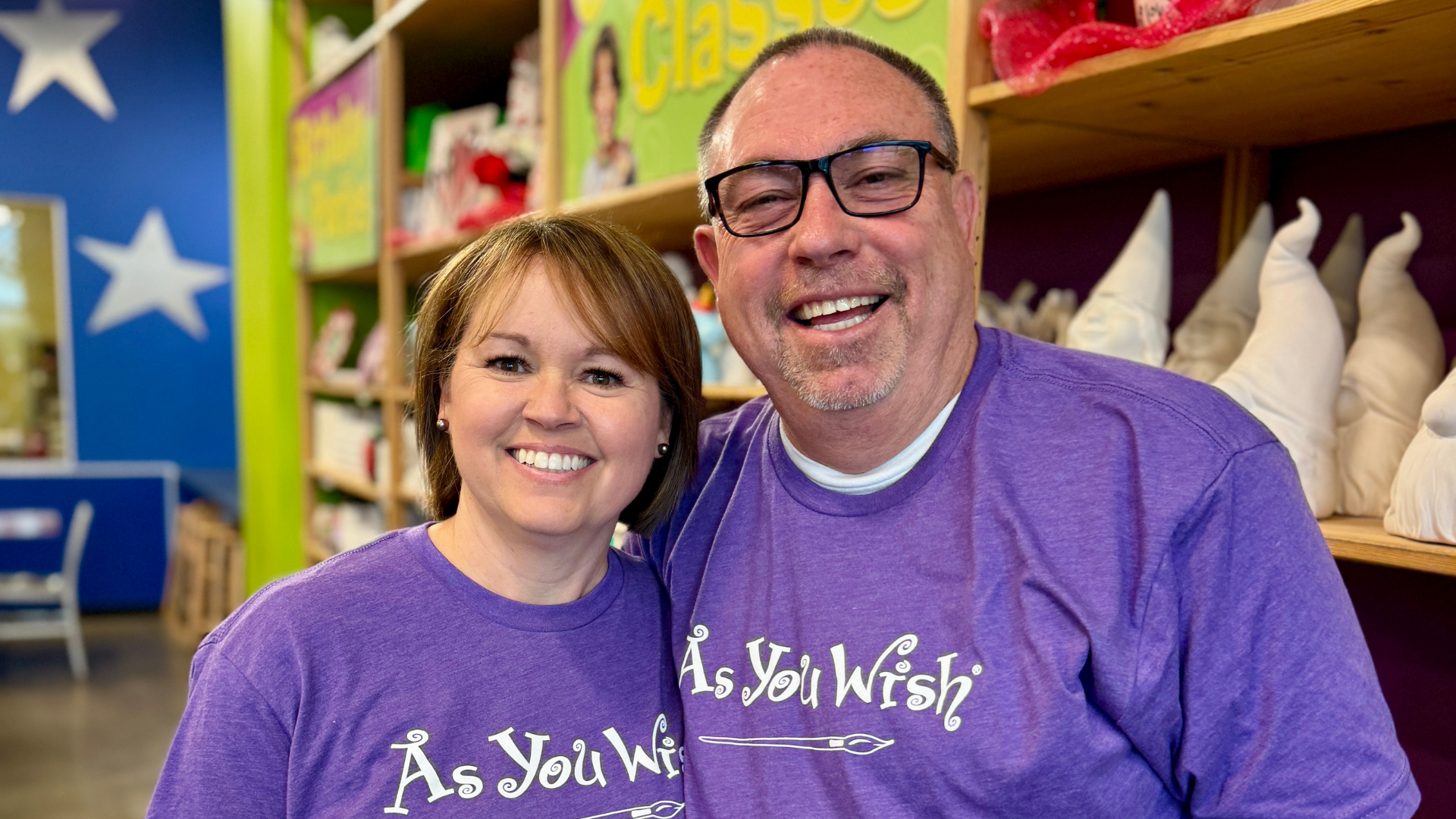 Two people wearing purple 'As You Wish' shirts in a store setting.