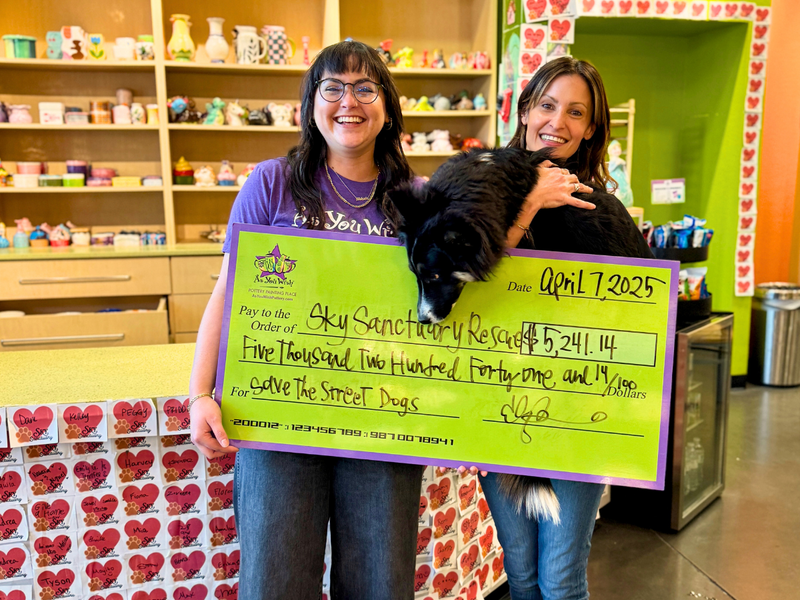Two women and a dog holding a large check in a store setting